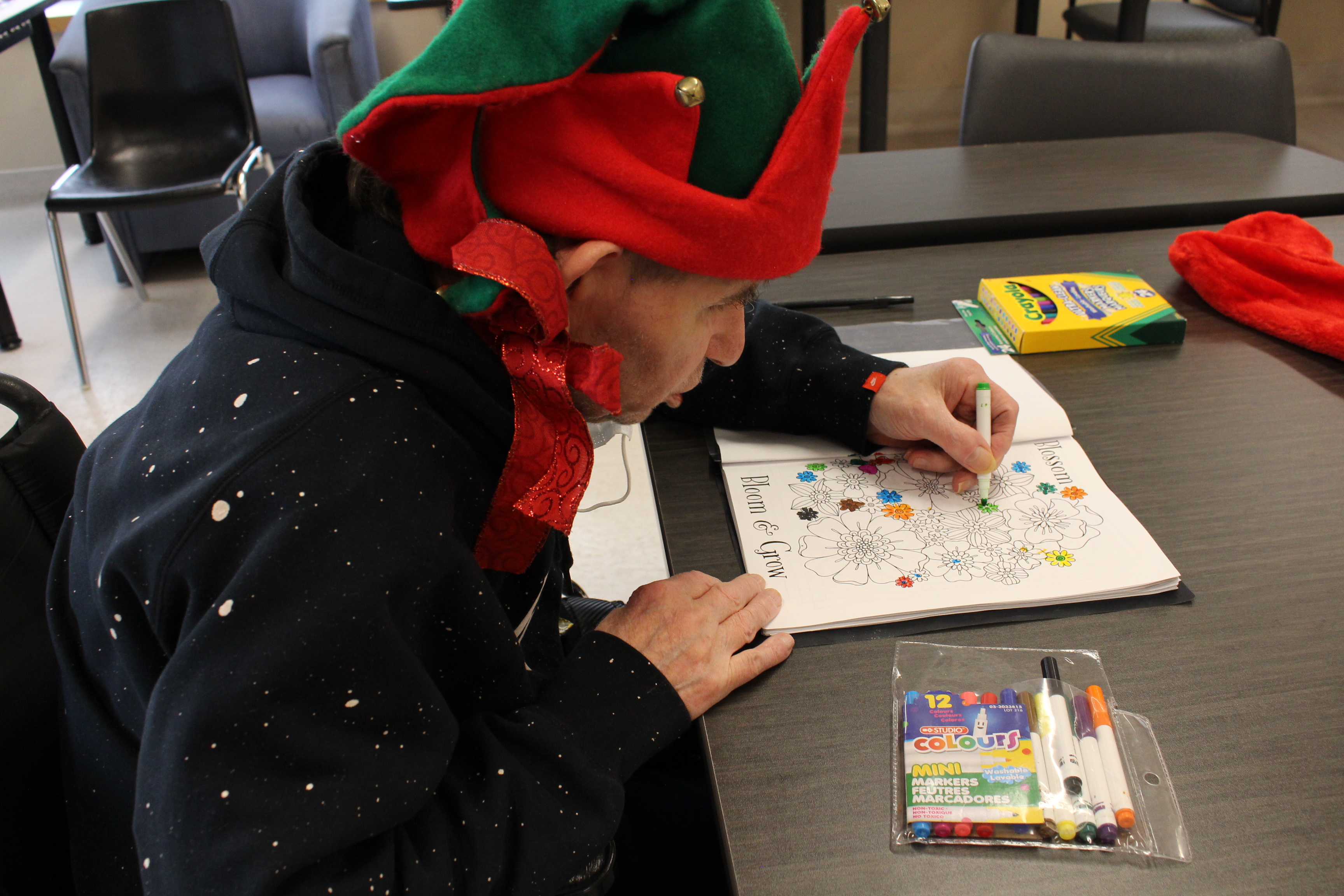 A man in an elf hat is seen colouring a picture of flowers.