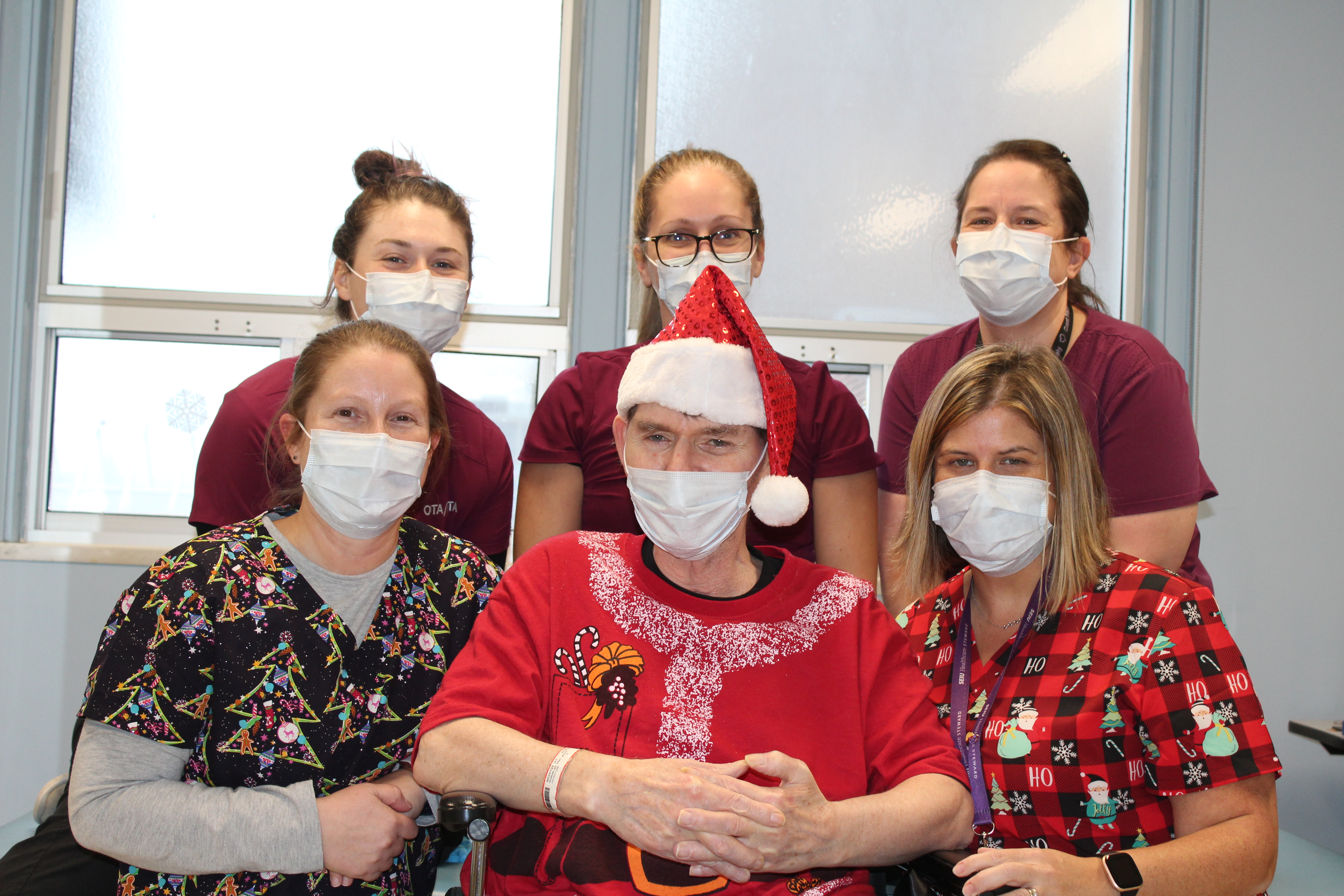 A group photo of 6 individuals; in the centre, a man wearing a festive shirt and a Santa hat.